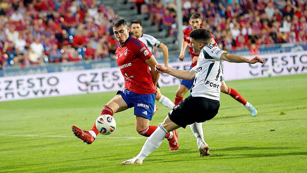 Dwóch piłkarzy walczących o piłkę na boisku, jeden w czerwonej koszulce, drugi w białej.