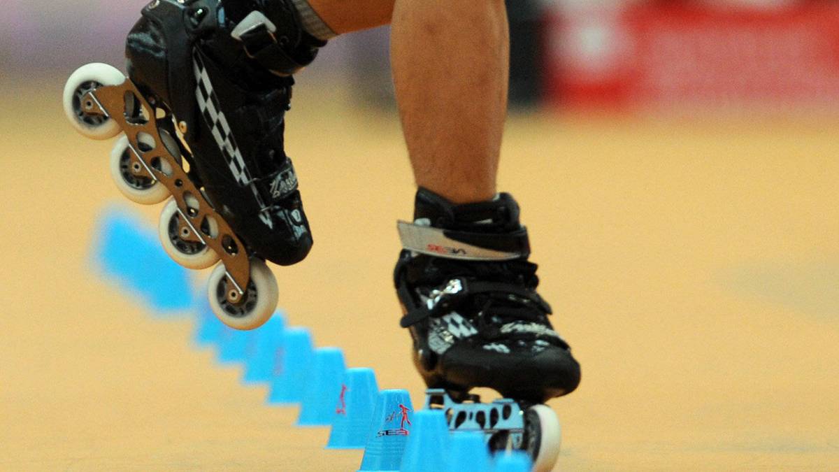 Zbliżenie na nogi osoby na rolkach freestyle inline wykonującej trik między niebieskimi pachołkami.