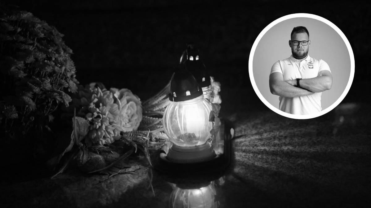 Monochromatyczne zdjęcie przedstawiające znicz palący się pośr&oacute;d kwiat&oacute;w, z małym portretem uśmiechniętego mężczyzny w okręgu po prawej stronie.