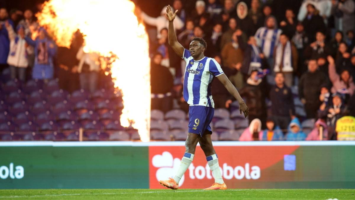 Piłkarz FC Porto w niebiesko-białej koszulce z numerem 9, idący po boisku z piłką u nogi, a za nim eksplozja ognia i tłum kibic&oacute;w na trybunach.