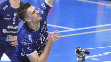 Siatkarz w niebieskim stroju z numerem 23 na plecach wykonuje zagrywkę.