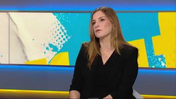 Kobieta w czarnej marynarce i koszuli siedzi i patrzy w bok.