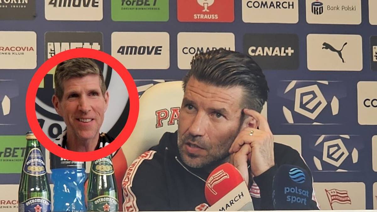 Zdjęcie przedstawia dw&oacute;ch mężczyzn na konferencji prasowej. Po prawej stronie siedzi mężczyzna z ręką przy uchu, m&oacute;wiący do mikrofonu. Po lewej stronie, w czerwonym okręgu, widoczny jest uśmiechnięty mężczyzna.