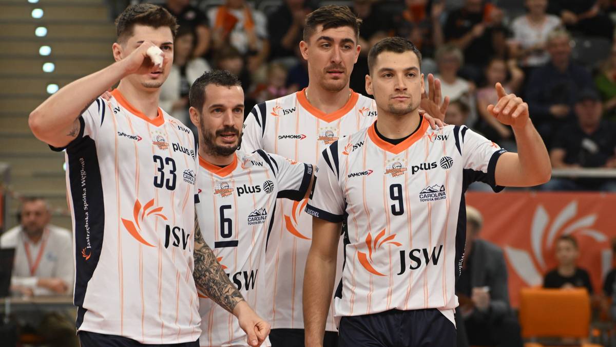 Czterech siatkarzy w identycznych strojach sportowych, jeden z nich pokazuje gest pozdrowienia, pozostałych dwóch wpatruje się przed siebie.