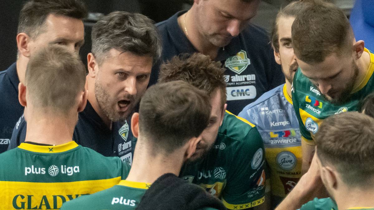 Grupa siatkarzy w zielono-ż&oacute;łtych strojach sportowych, jeden z nich, być może trener, intensywnie przemawia do zespołu, skupiając uwagę zawodnik&oacute;w.