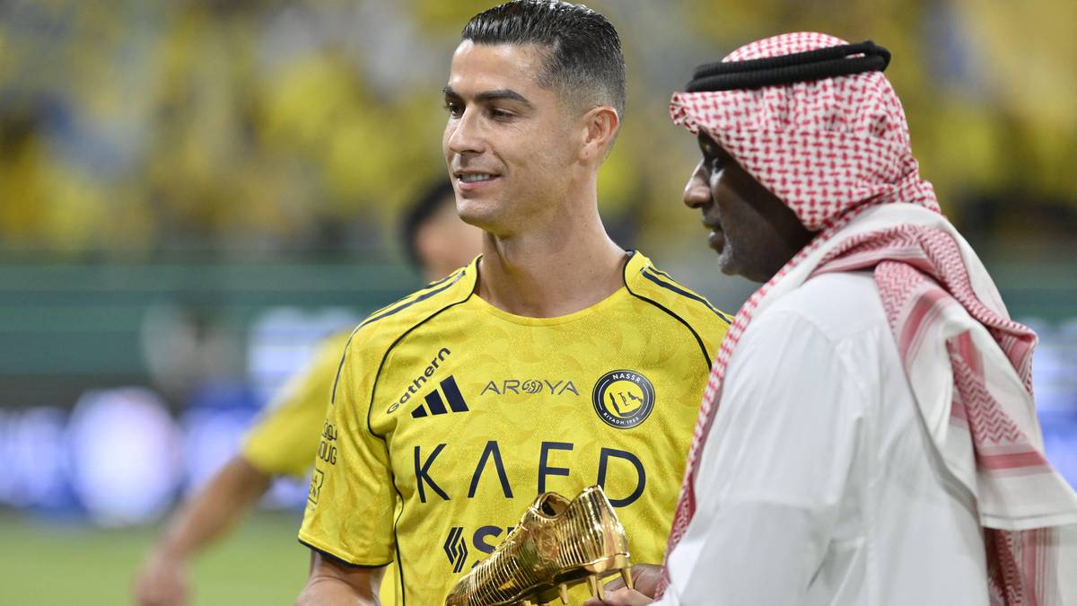 Piłkarz Cristiano Ronaldo w żółtej koszulce z trofeum w dłoniach, rozmawia z mężczyzną w tradycyjnym arabskim stroju.