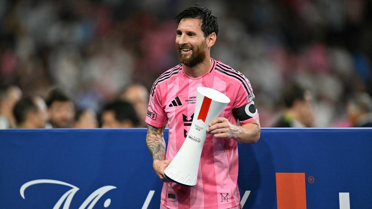 Lionel Messi w różowej koszulce trzyma trofeum.