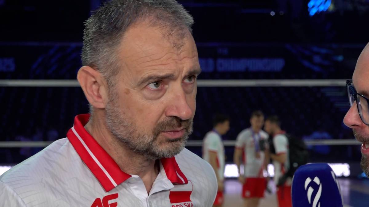 Nikola Grbić, trener reprezentacji Polski w siatkówce, w białej koszulce z czerwonym kołnierzykiem, patrzy w bok z lekkim zmarszczeniem brwi.