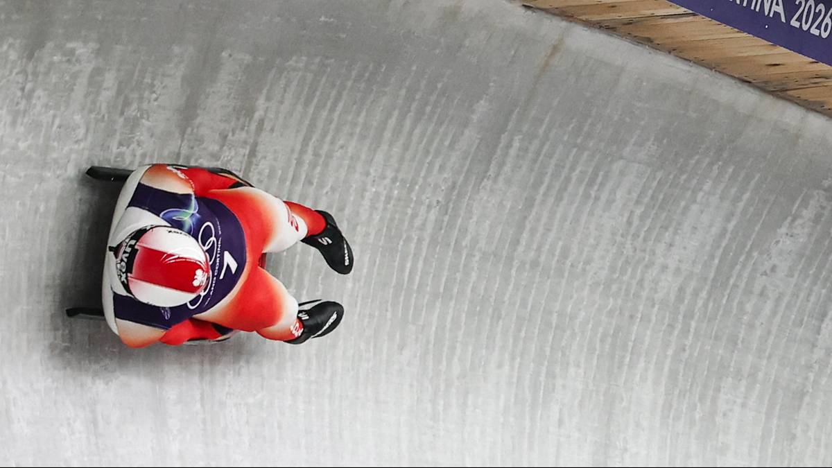 Saneczkarz w kasku i kombinezonie z flagą Wielkiej Brytanii wjeżdża na zakręt toru saneczkowego.