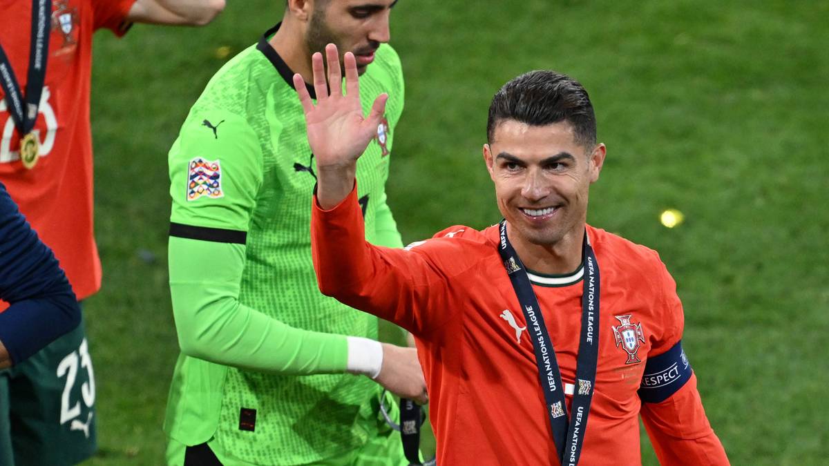 Piłkarz w pomarańczowej koszulce macha do widza, obok stoi bramkarz w zielonej koszulce.