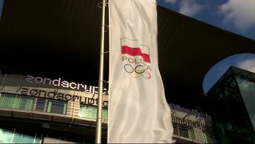 Flaga z godłem Polski i pierścieniami olimpijskimi powiewa przed budynkiem z napisem "zondacrypt".