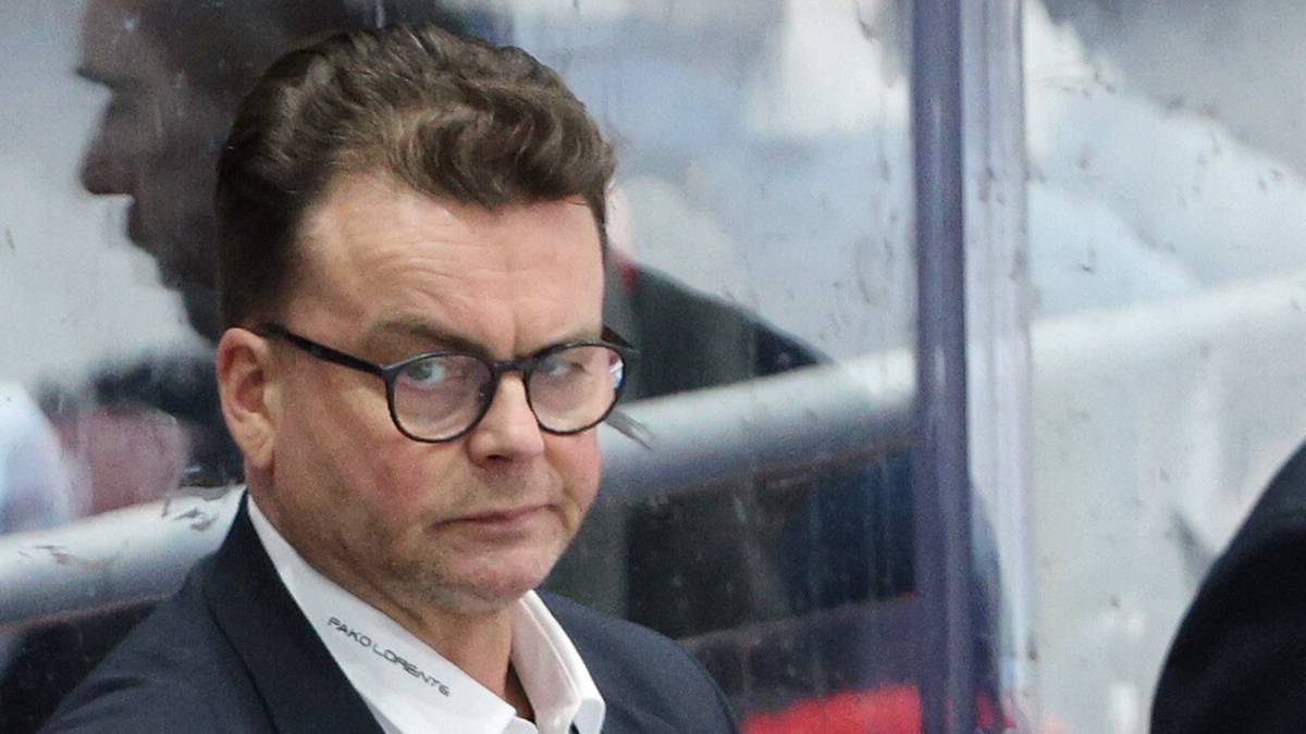 Trzech mężczyzn w garniturach na ławce rezerwowych drużyny hokejowej.