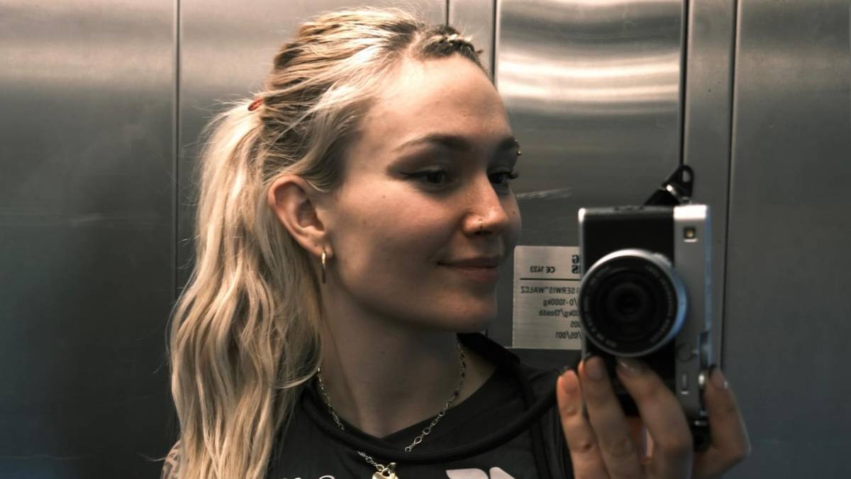 Młoda kobieta z blond włosami spiętymi w kucyk, robiąca sobie zdjęcie aparatem.