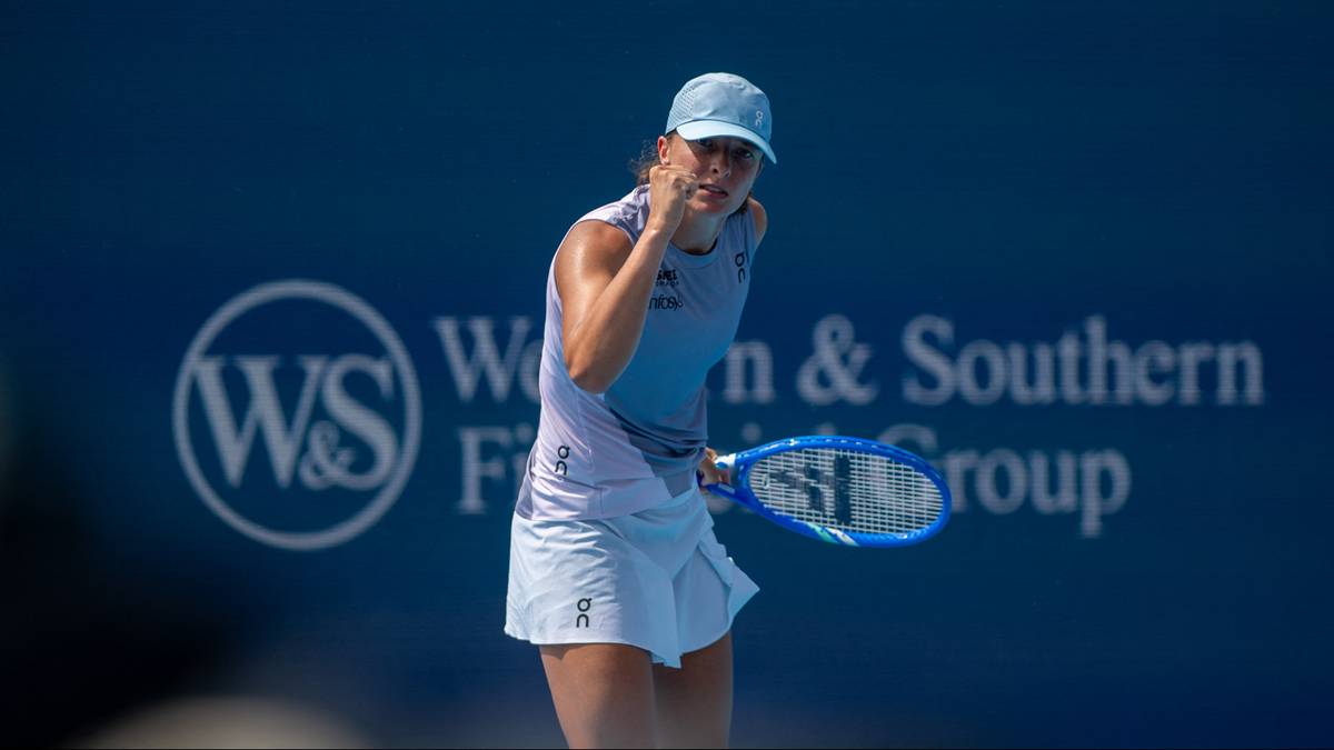 Iga Świątek, polska tenisistka, w białej koszulce i spódnicy oraz niebieskiej czapce, na korcie tenisowym, trzymająca rakietę.