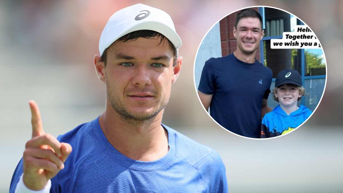 Tenisista Hubert Hurkacz w białej czapce i niebieskiej koszulce z charakterystycznym gestem uniesionego palca.