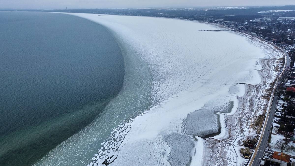 Widok z lotu ptaka na zamarznięte wybrzeże morza z lodem przy brzegu i zabudową miejską w oddali.