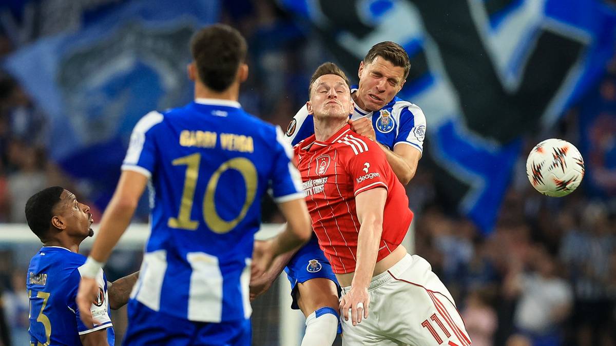 Piłkarze w niebiesko-białych strojach i w czerwonych strojach rywalizują o piłkę podczas meczu.