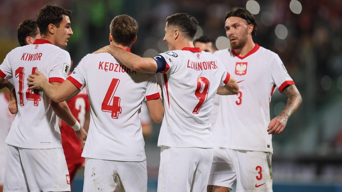 Piłkarze reprezentacji Polski w białych strojach meczowych podczas rozmowy na boisku.