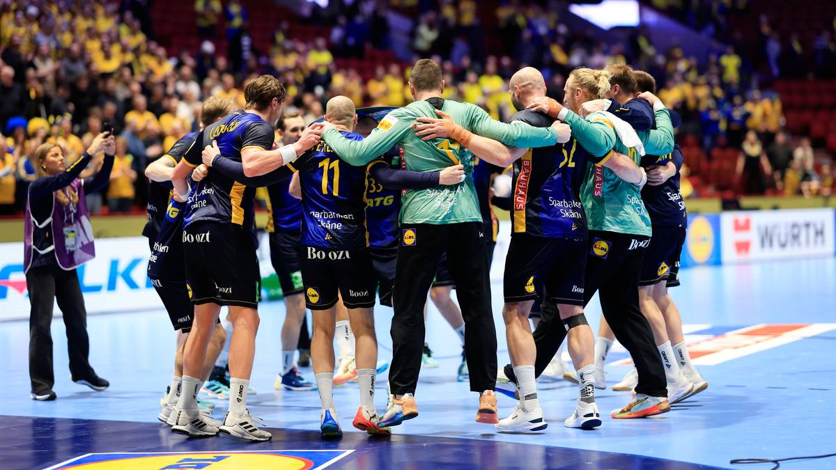 Drużyna piłkarzy ręcznych w zielonych strojach świętuje w uścisku na boisku sportowym, z kibicami na trybunach w tle.