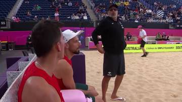 Trener siatkówki plażowej w czarnej koszulce i spodenkach udziela wskazówek zawodnikom.