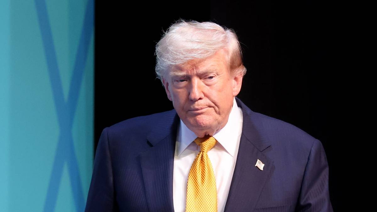 Donald Trump w ciemnoniebieskim garniturze i ż&oacute;łtym krawacie, patrzący na wprost z lekko zmarszczonymi brwiami.