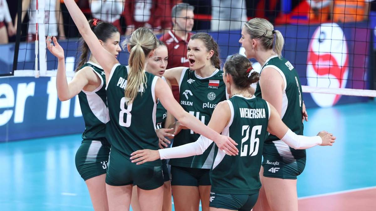 Grupa siatkarek w zielonych strojach sportowych stoi blisko siebie, przytulając się i rozmawiając podczas przerwy w meczu.
