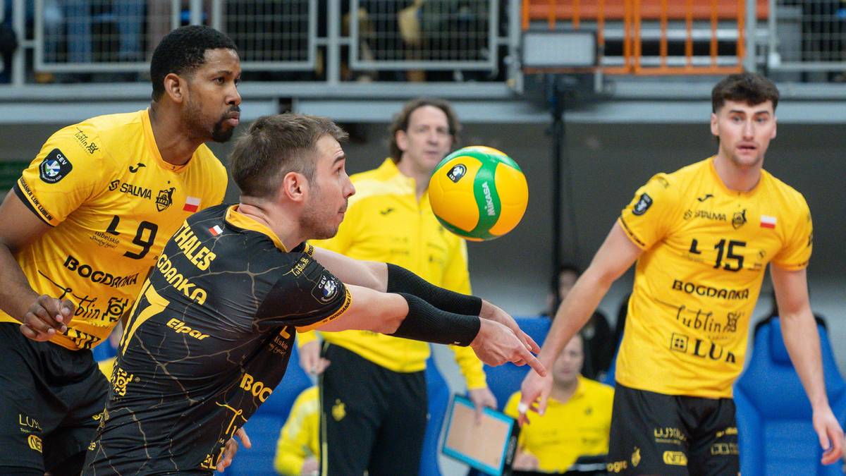 Siatkarze w akcji podczas meczu PlusLigi, jeden z zawodnik&oacute;w zagrywa piłkę.