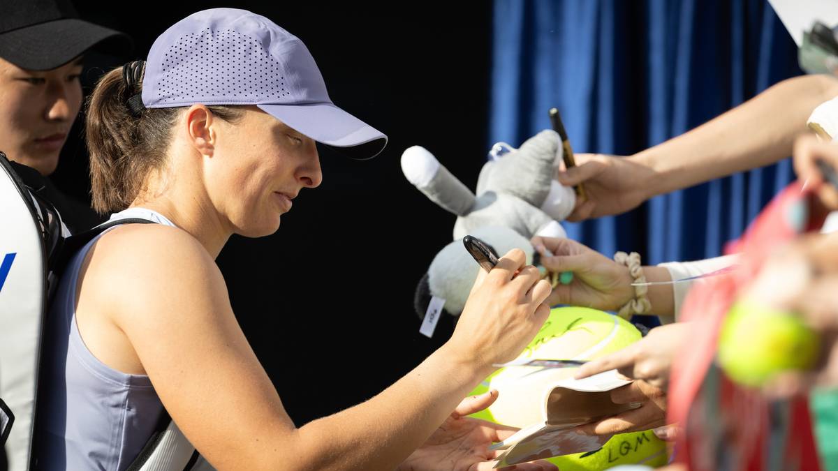 Tenisistka w czapce z daszkiem podpisuje pluszową zabawkę i piłkę tenisową.