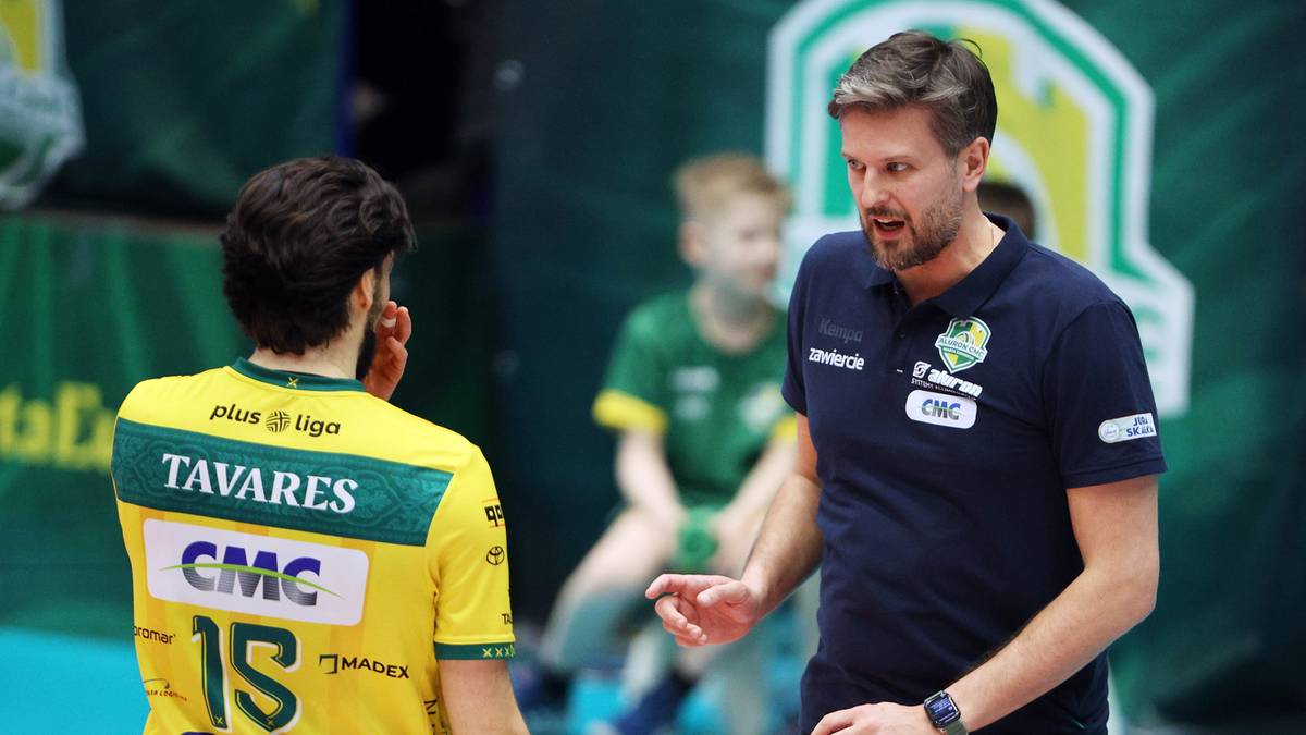 Siatkarz w ż&oacute;łtej koszulce i trener w granatowej koszulce rozmawiają na boisku.
