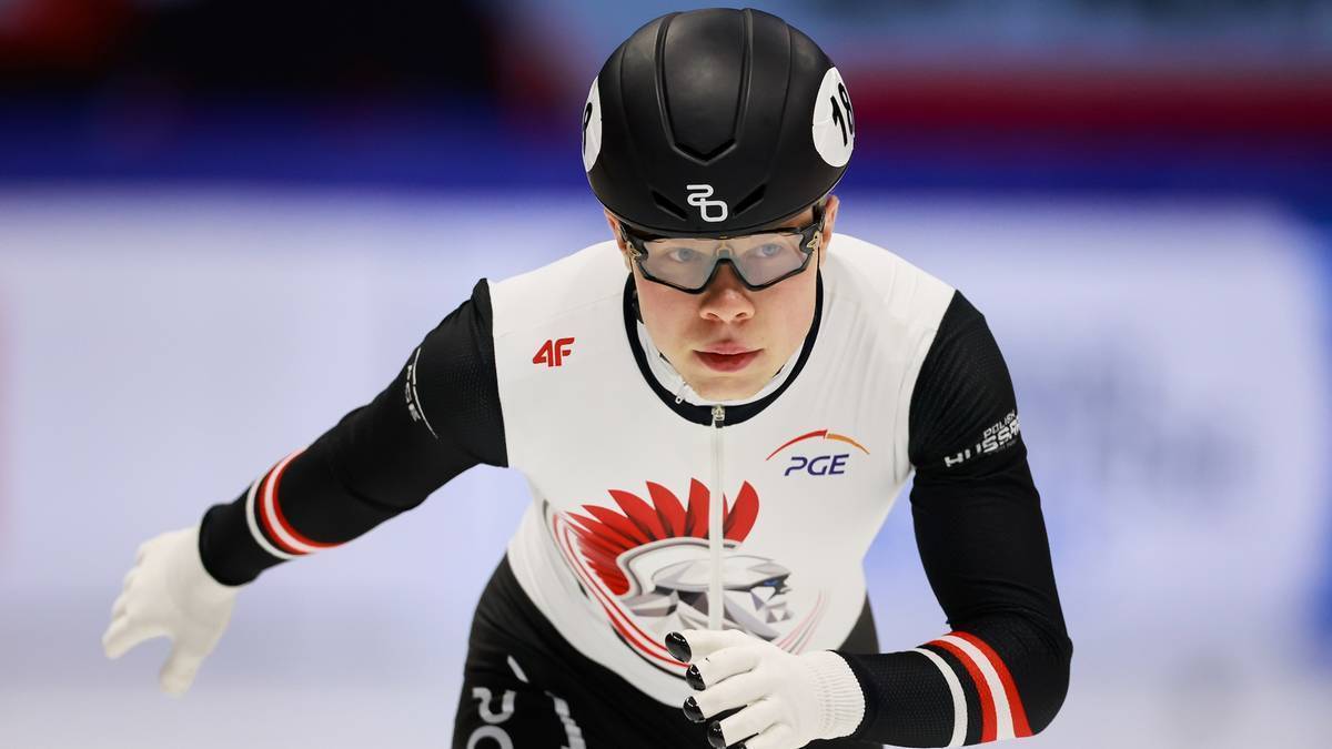 Zawodnik short tracku w kasku i goglach, w białej kamizelce z czarnymi rękawami i logo PGE.