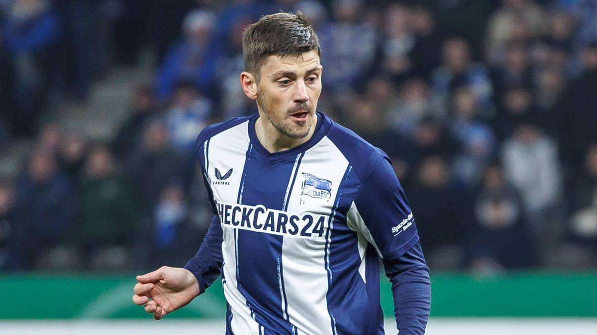 Piłkarz w niebiesko-białym stroju biegnie po boisku w kierunku bramkarza w ż&oacute;łtym stroju.