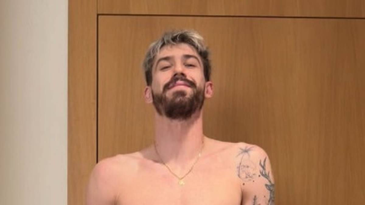 Młody mężczyzna z zarostem i blond włosami na tle drewnianych drzwi.