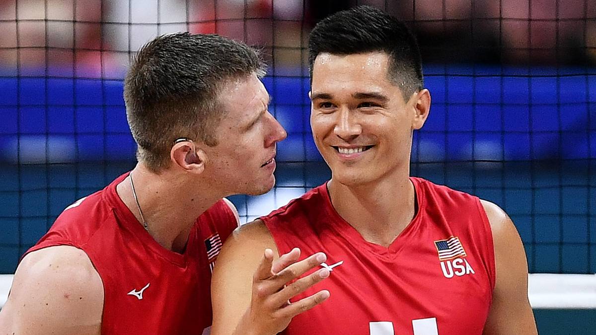 Dw&oacute;ch siatkarzy w czerwonych strojach z białymi numerami na plecach, jeden z nich, Micah Christenson z numerem 11, uśmiecha się i patrzy na drugiego siatkarza.