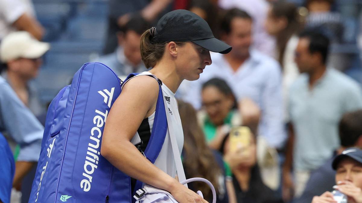 Iga Świątek z niebieską torbą tenisową z logo "Tecnifibre" na ramieniu, w czapce z daszkiem, zmierza w prawo.