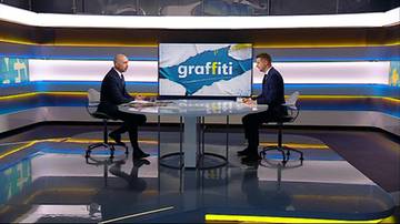 Dw&oacute;ch mężczyzn w garniturach siedzi naprzeciwko siebie przy okrągłym stole w studiu telewizyjnym.