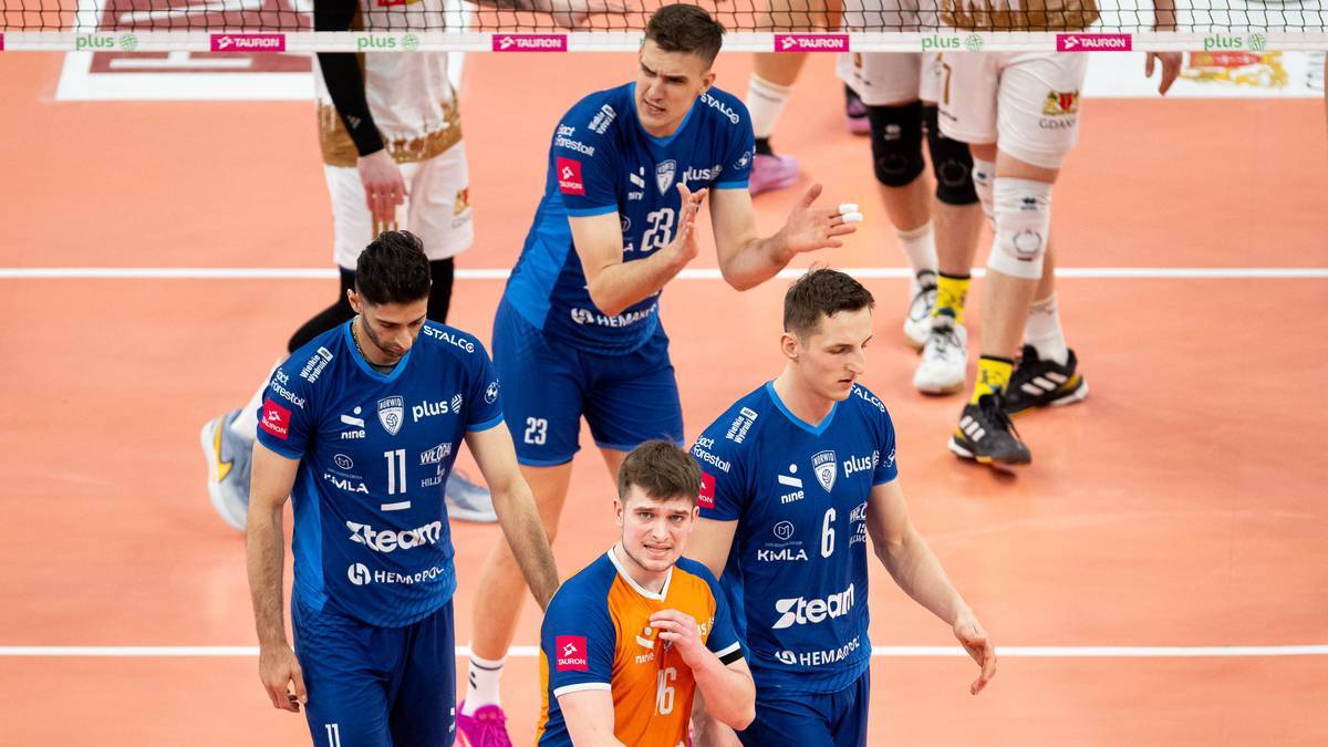 Grupa siatkarzy w niebieskich strojach meczowych, z numerami na koszulkach, na tle pomarańczowego boiska.