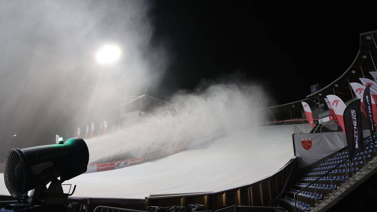 Armatka śnieżna wyrzuca sztuczny śnieg na skocznię narciarską nocą.
