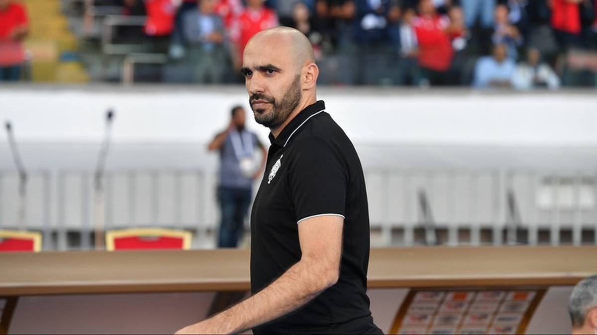 Walid Regragui, trener reprezentacji Maroka, w czarnej koszulce polo na tle trybun stadionu.