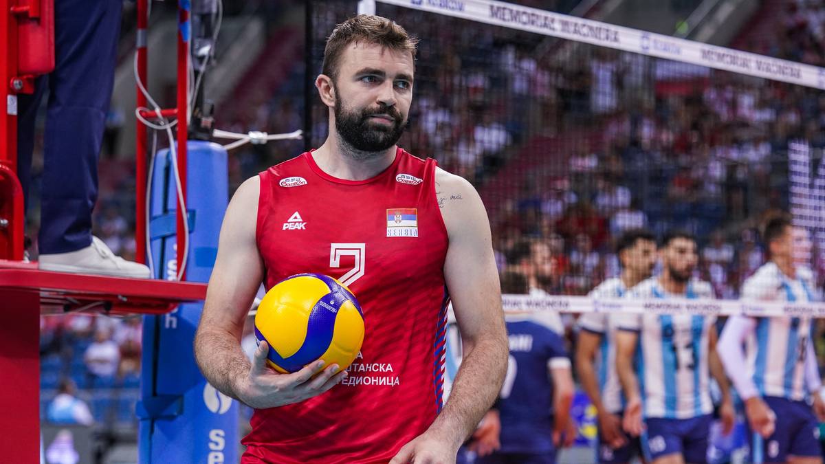 Siatkarz w czerwonej koszulce z numerem 2 trzyma piłkę do siatkówki.