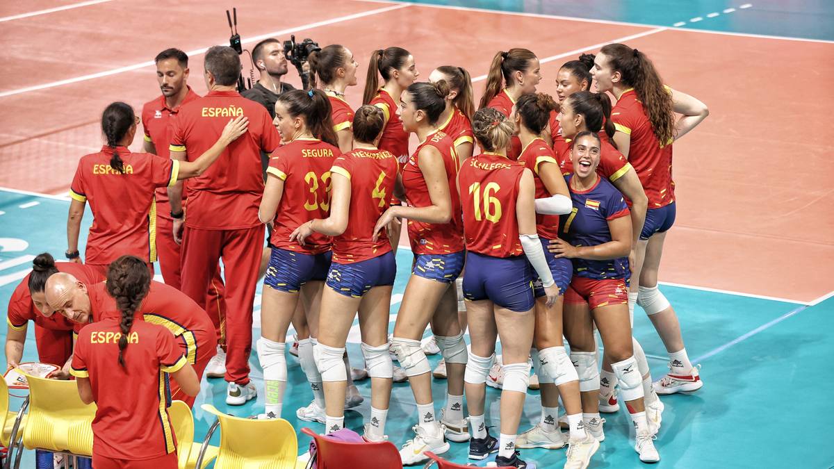 Drużyna siatkarek w czerwonych strojach zebrała się w kółku, rozmawiając między sobą.