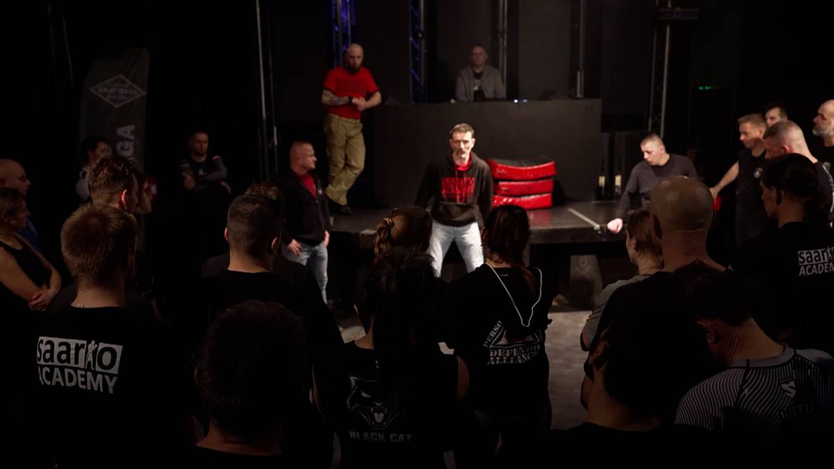 Grupa osób na szkoleniu samoobrony Defendo, prowadzący szkolenie stoją przed uczestnikami.