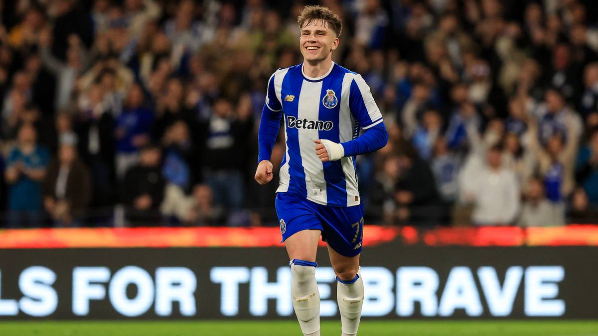 Piłkarz FC Porto w niebiesko-białym stroju biegający po boisku, uśmiechnięty, trybuny kibic&oacute;w w tle.