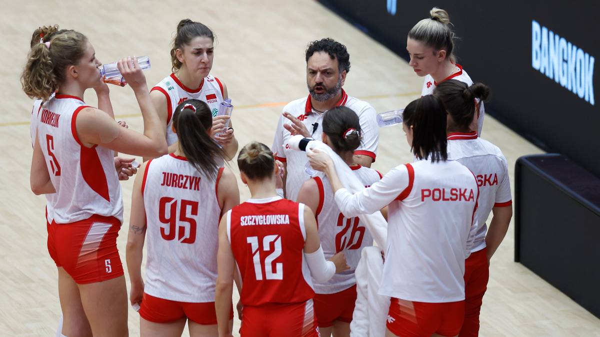 Dopojęciowe kobiety w strojach siatkarskich w czerwono-białych barwach i trener dyskutują na parkiecie.