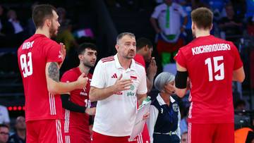 Siatkarze w czerwonych strojach z numerami na plecach i trener w białej koszulce z czerwonymi elementami.