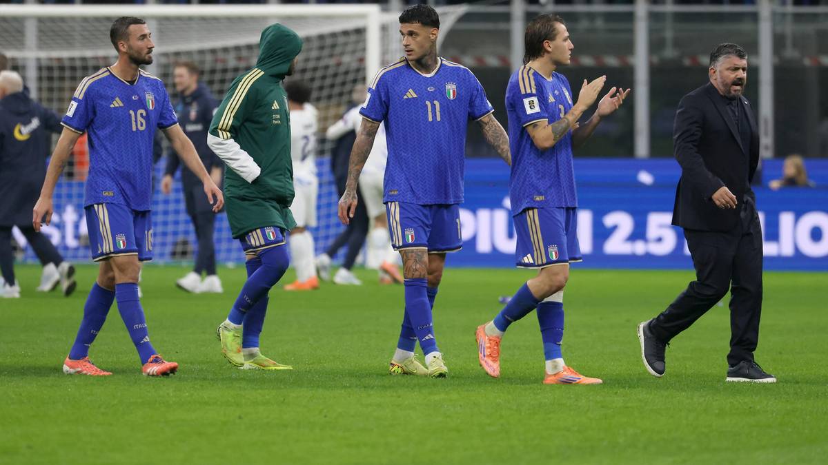 Piłkarze w niebieskich strojach idący po boisku, jeden w zielonej bluzie z kapturem, w tle trybuny z kibicami.