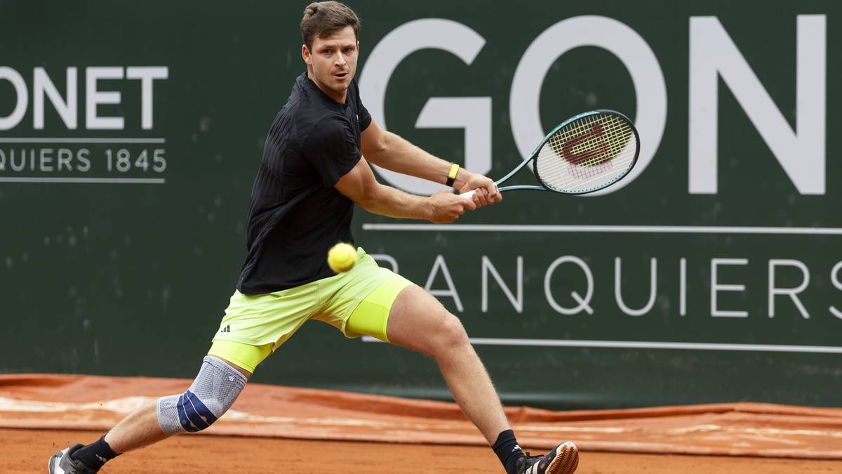 Hubert Hurkacz, polski tenisista, podczas uderzenia forhendowego na korcie tenisowym. Ma na sobie czarną koszulkę, ż&oacute;łte spodenki, opaskę kompresyjną na kolanie i ciemne buty. Jest w trakcie meczu.