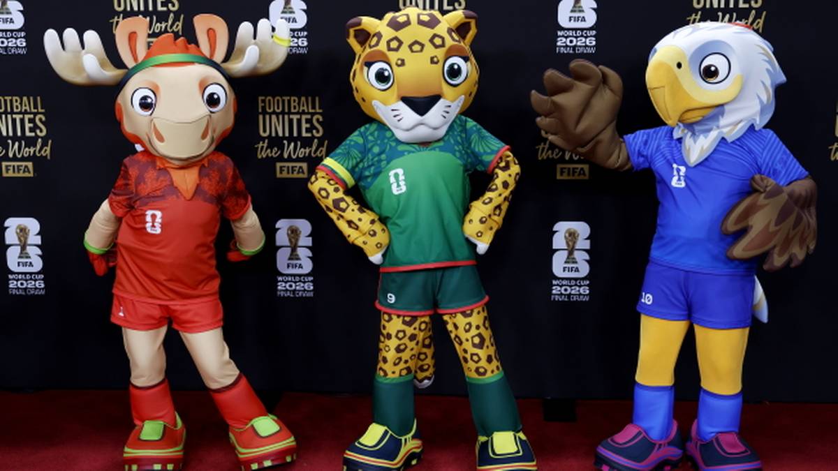 Trzy maskotki w strojach sportowych stoją obok siebie na czerwonym dywanie.