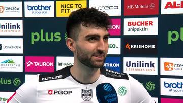 Portret mężczyzny w stroju sportowym, z widocznymi logotypami sponsorów w tle.