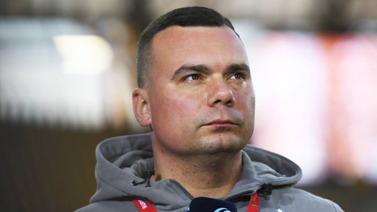 Portret mężczyzny z krótkimi włosami, w bluzie z kapturem, spoglądającego w bok z wyrazem koncentracji na twarzy.