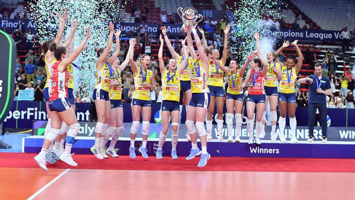 Drużyna siatkarska świętuje zwycięstwo, unosząc puchar i rzucając konfetti.